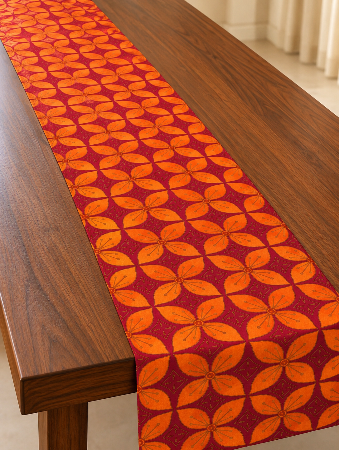 Orange floral motifs on a maroon dupion silk table runner draped along a wooden dining table.